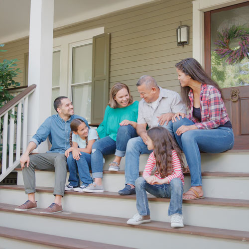 Multigenerational family smiling together on the front porch steps of their home